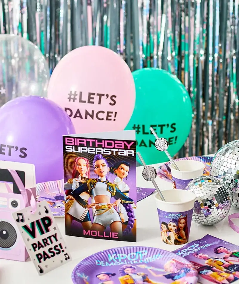Close-up of a dance-themed kids party setup with Let’s Dance balloons, a Birthday Superstar card, disco balls, themed cups and plates, and colorful party decorations on a white table.